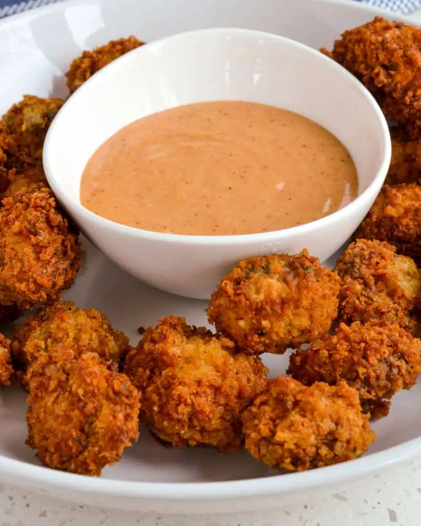 Fried mushrooms on a plate with a bowl of dipping sauce. 