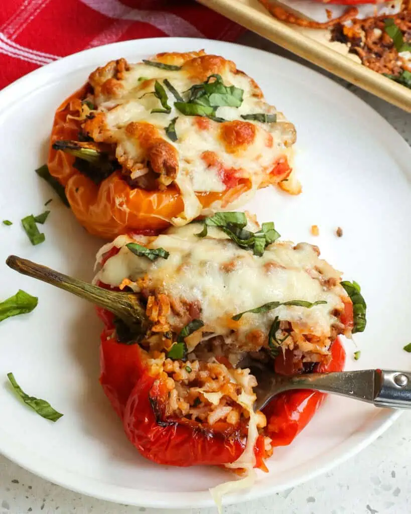 Baked stuffed bell peppers on a serving plate with a fork. 