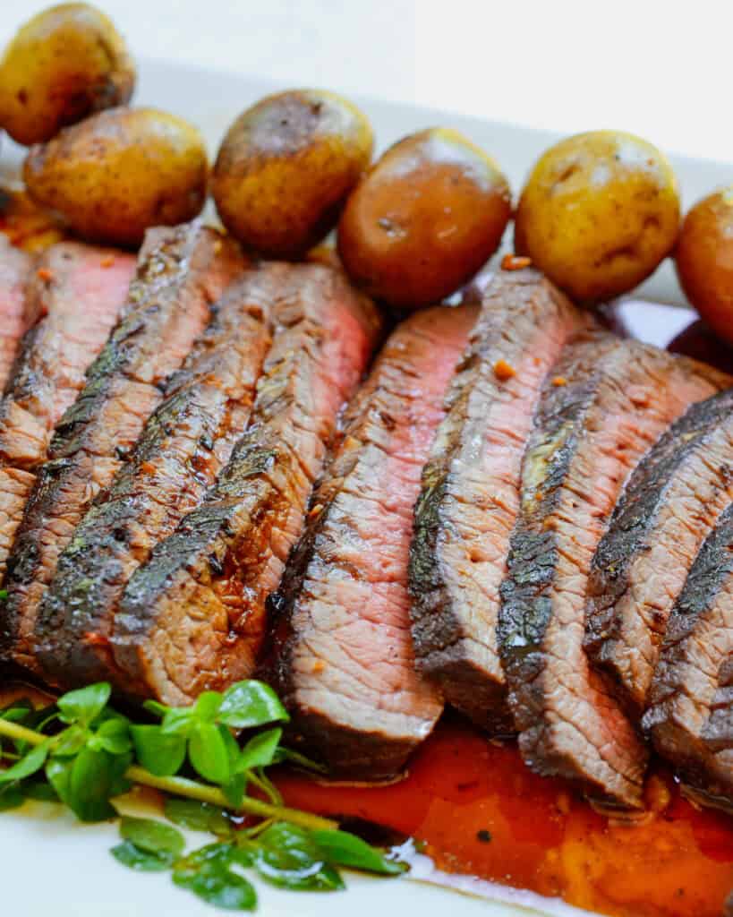 Sliced london broil steak on a plate with  baby Yukon gold potatoes. 