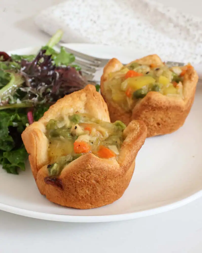 Two mini chicken pots pies on a plate with mixed spring greens. 