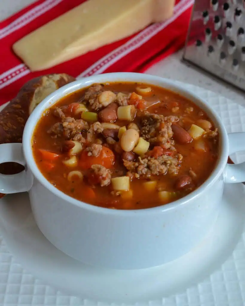 Overhead view of a soup crock full of pasta e fagioli with a piece of crusty bread. 