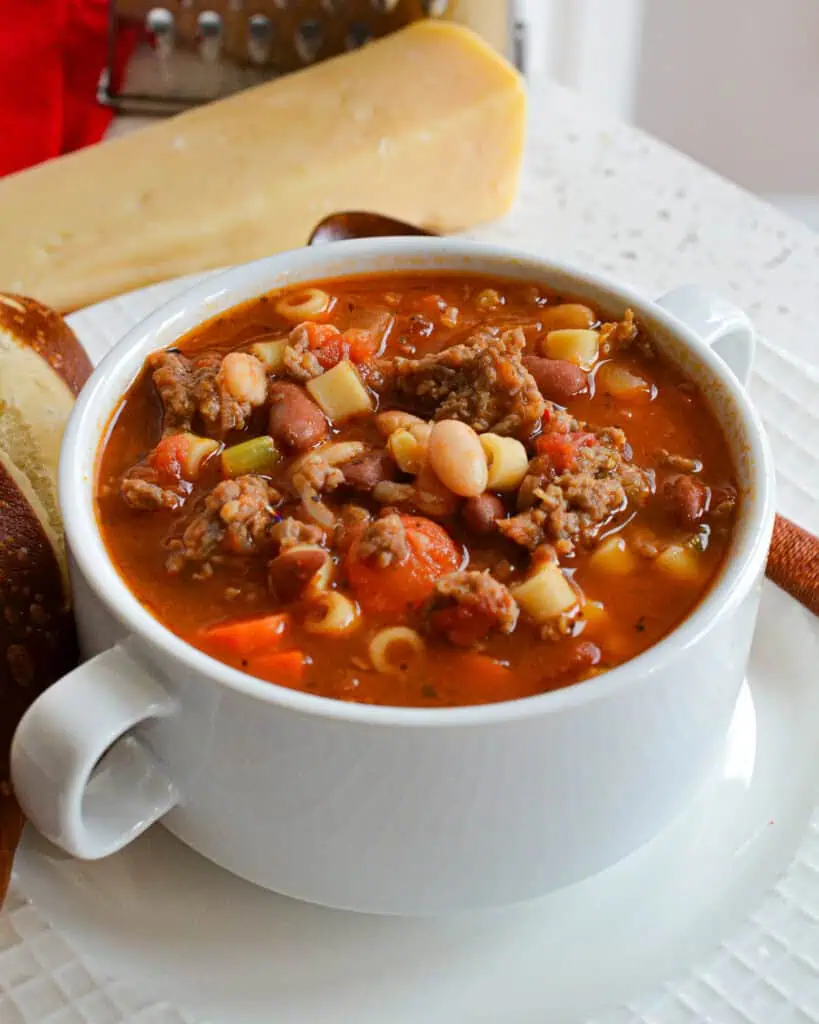 A bowl of pasta e fagioli with a block of Parmesan cheese and a cheese grater in the background. 