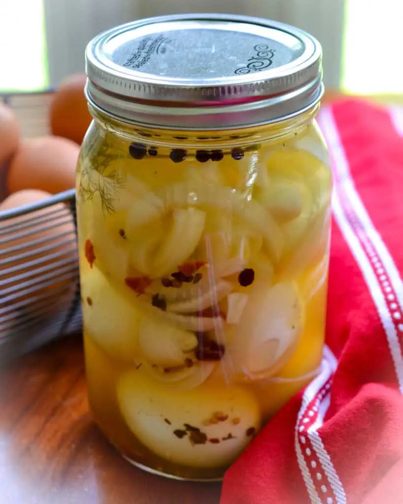 Pickled eggs in a large mason jar with fresh eggs in the background. 