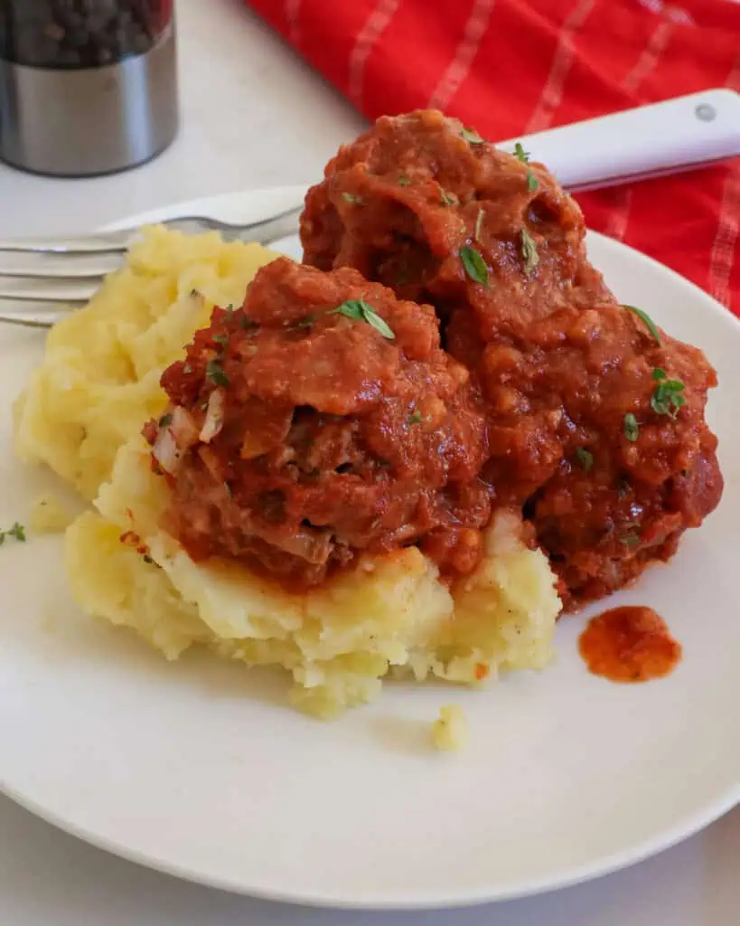 Porcupine meatballs over mashed potatoes on a plate with salt and pepper shaker in the background. 