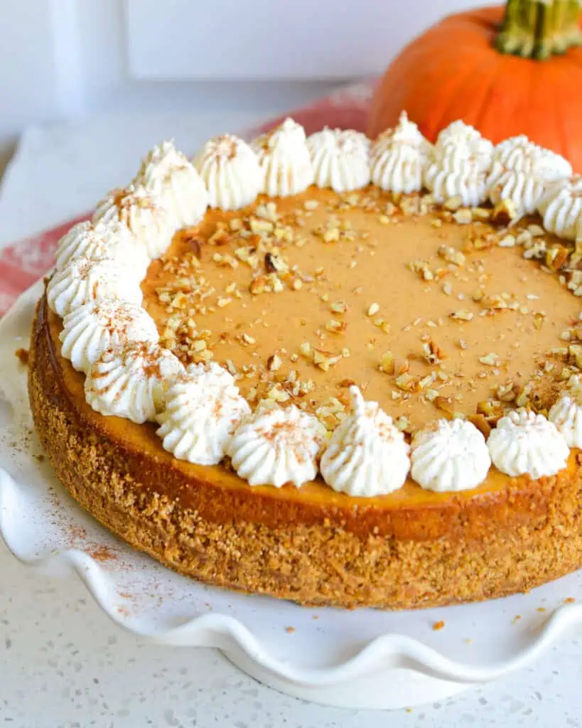 A whole pumpkin cheesecake on a stand with a pumpkin in the background. 