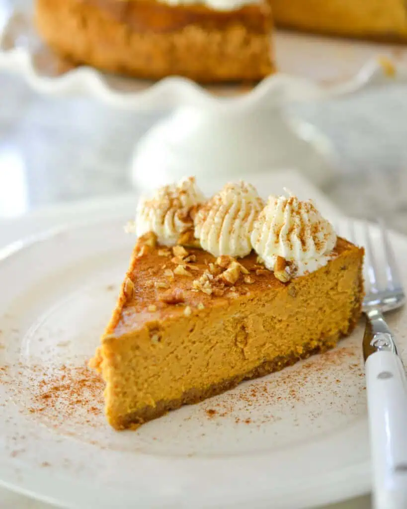 A slice of pumpkin cheesecake topped with whipped cream and pecans on a plate with a fork. 