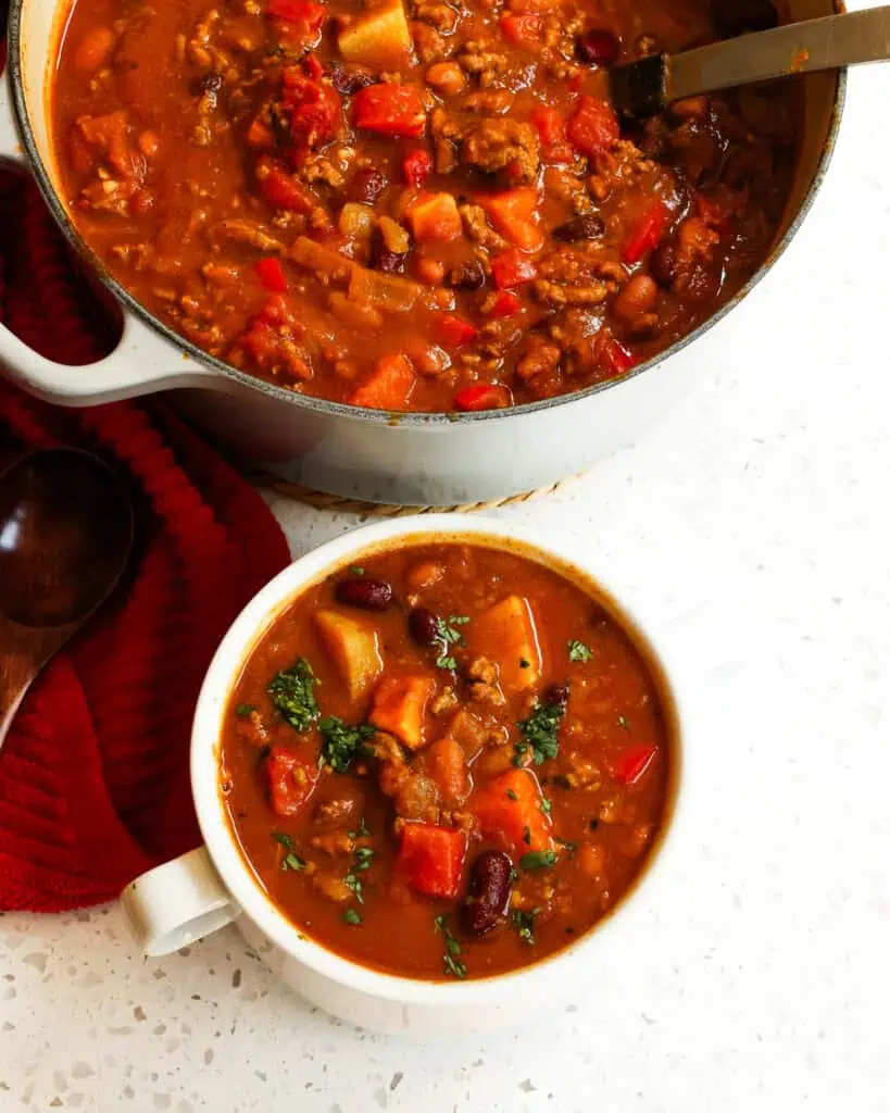 An overhead image of a Dutch oven and bowl full of pumpkin chili. garnished with cilantro.