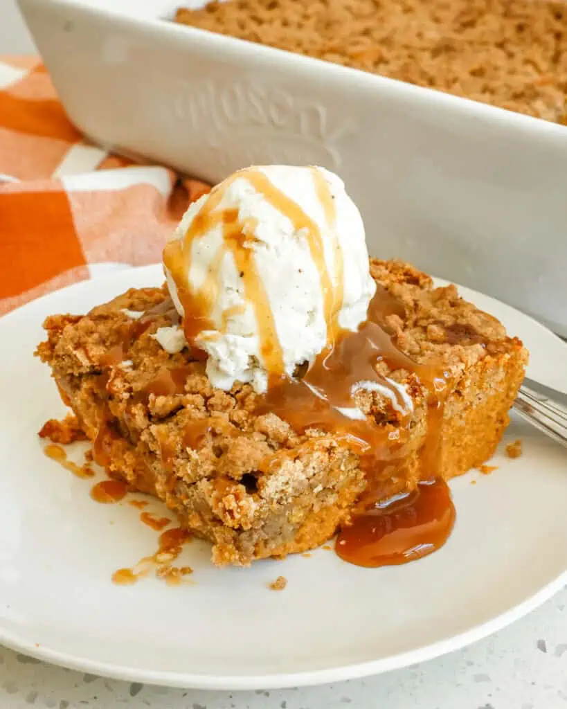 A single serving of pumpkin dump cake served a la mode on a small round plate wth a fork. 