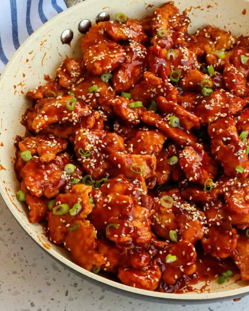 Sesame chicken garnished toasted sesame seeds and sliced green onions in a large skillet. 