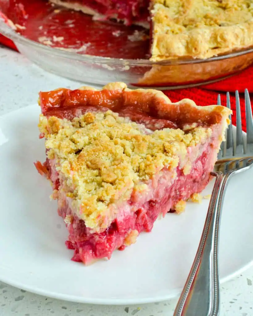 A single piece of strawberry rhubarb pie  on a round plate with a fork on it. 