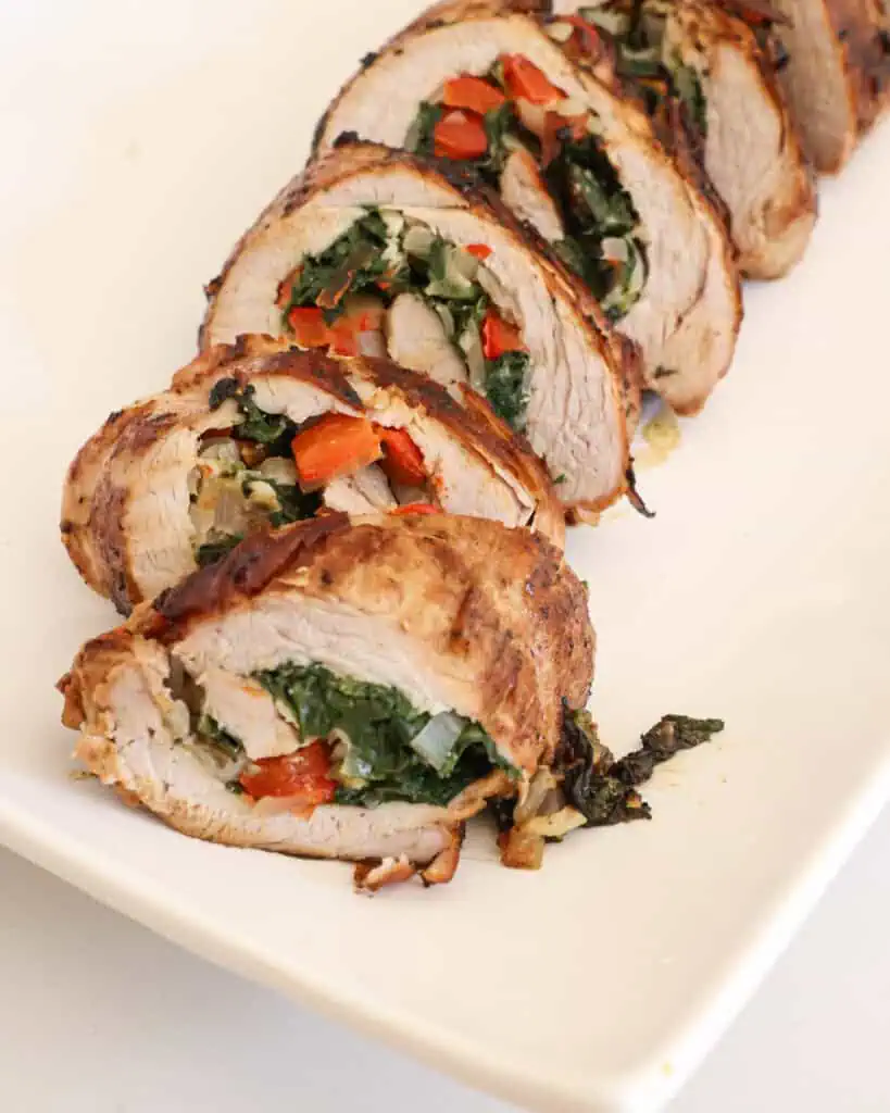 A close up view of stuffed pork tenderloin on a large serving platter. 