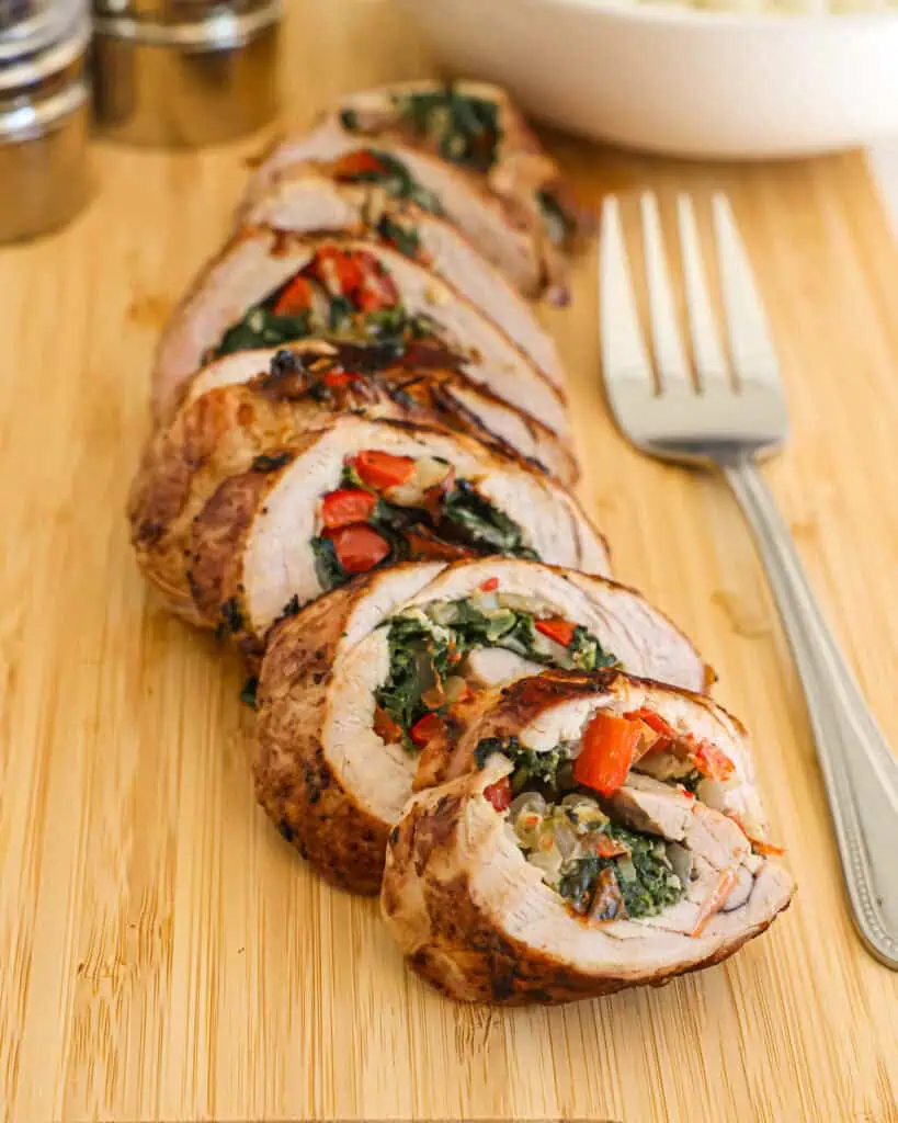 Sliced stuffed pork tenderloin on a wooden cutting board. 