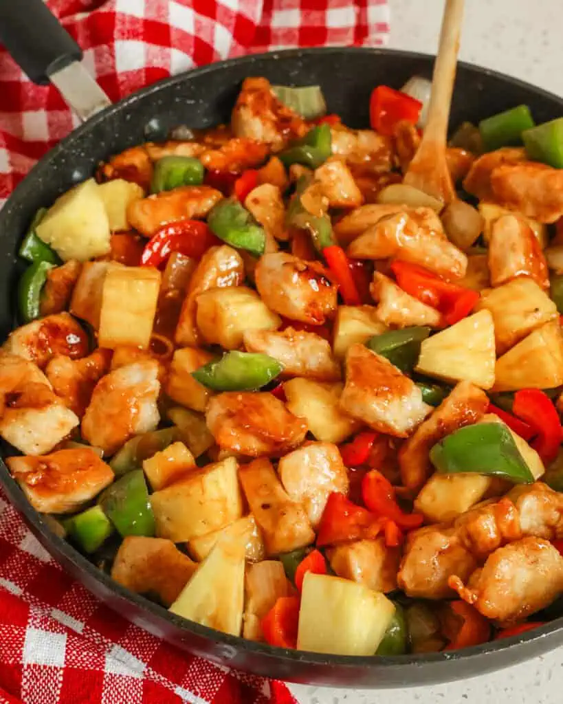 Sweet and sour chicken in a large skillet with wooden spoon. 