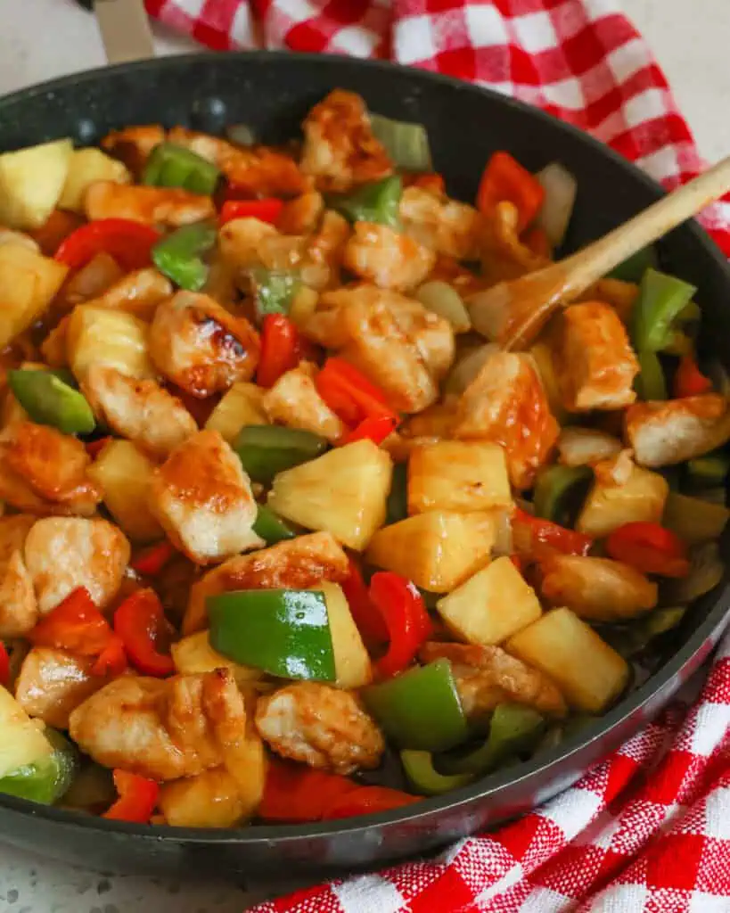 Sweet and sour chicken in a skillet with a wooden spoon. 