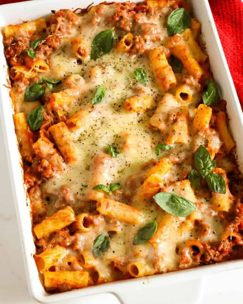 A large casserole dish with baked mostaccioli topped with melted mozzarella and fresh basil. 