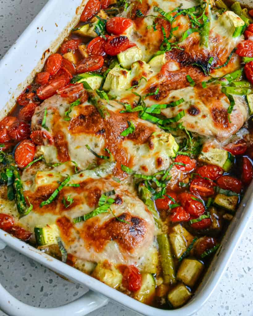 Casserole of baked chicken with tomatoes, asparagus, and zucchini topped with mozzarella. 