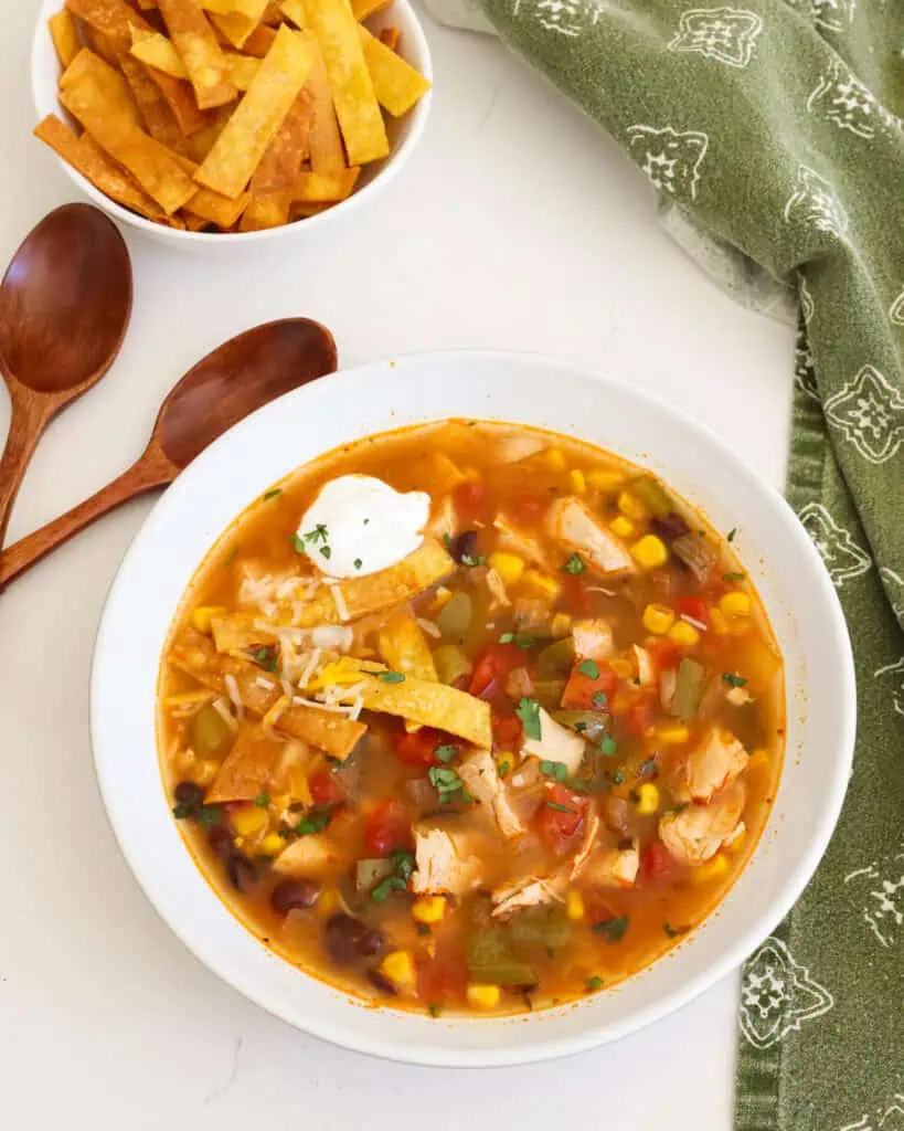 Chicken enchilada soup in a bowl with sour cream, cheese, and tortilla strips. 