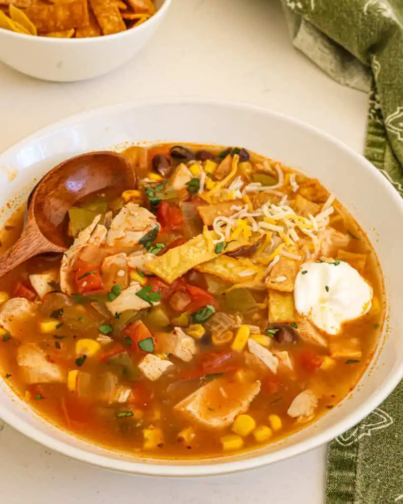 Chicken enchilada soup in a bowl with tortilla strips, sour cream, and shredded cheese. 