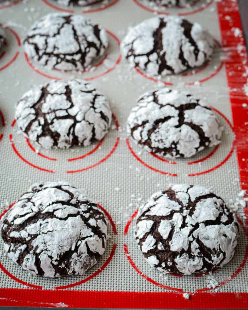 Freshly baked chocolate crinkle cookies on a silicone mat. 