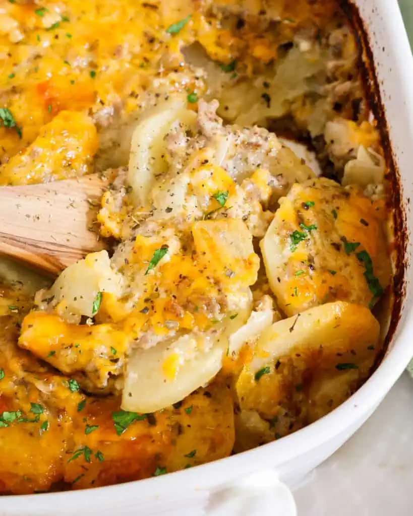 Cheesy hamburger and potatoes in an oval casserole dish with a wooden spoon. 