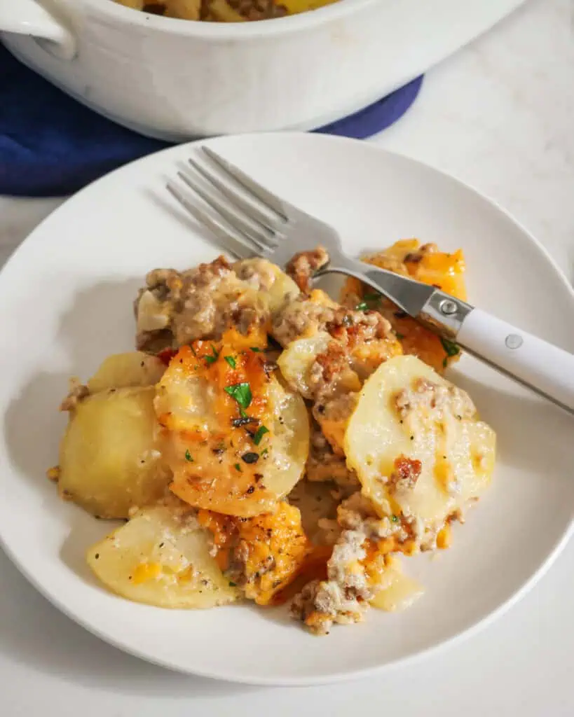 A plate full of hamburger and potato casserole with a fork in the background. 