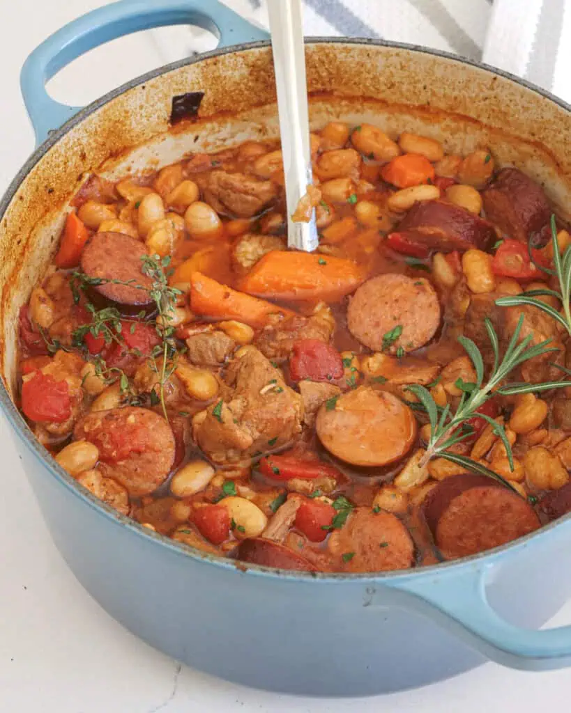 A Dutch oven full of cassoulet. A traditinal French stew that combines bacon, smoked pork sausage, and tender pork butt. All are slow-cooked with vegetables, tomatoes, beans, and fresh herbs.