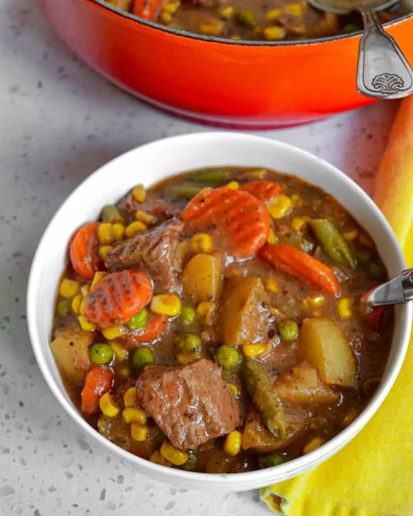 A bowl full of Mulligan stew tender stew meat, potatoes, corn, carrots, peas, green beans, and a perfect blend of  spices. 