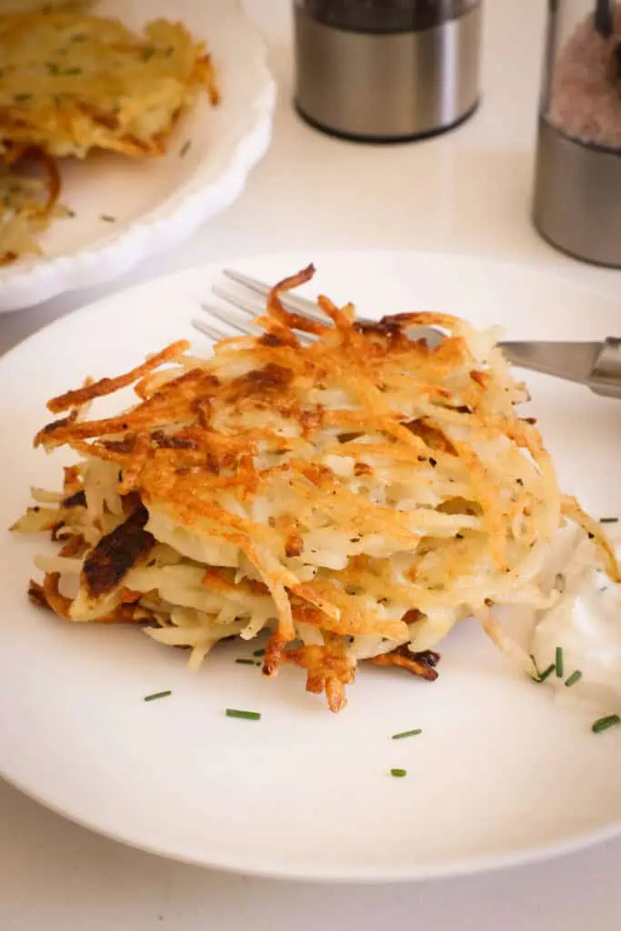 Stacked potato cakes on a single serving plate with sour cream and chives. 