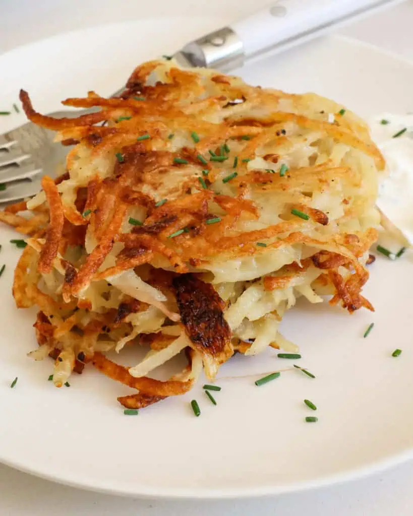 Three crispy pancakes on a plate with chives and a fork. 