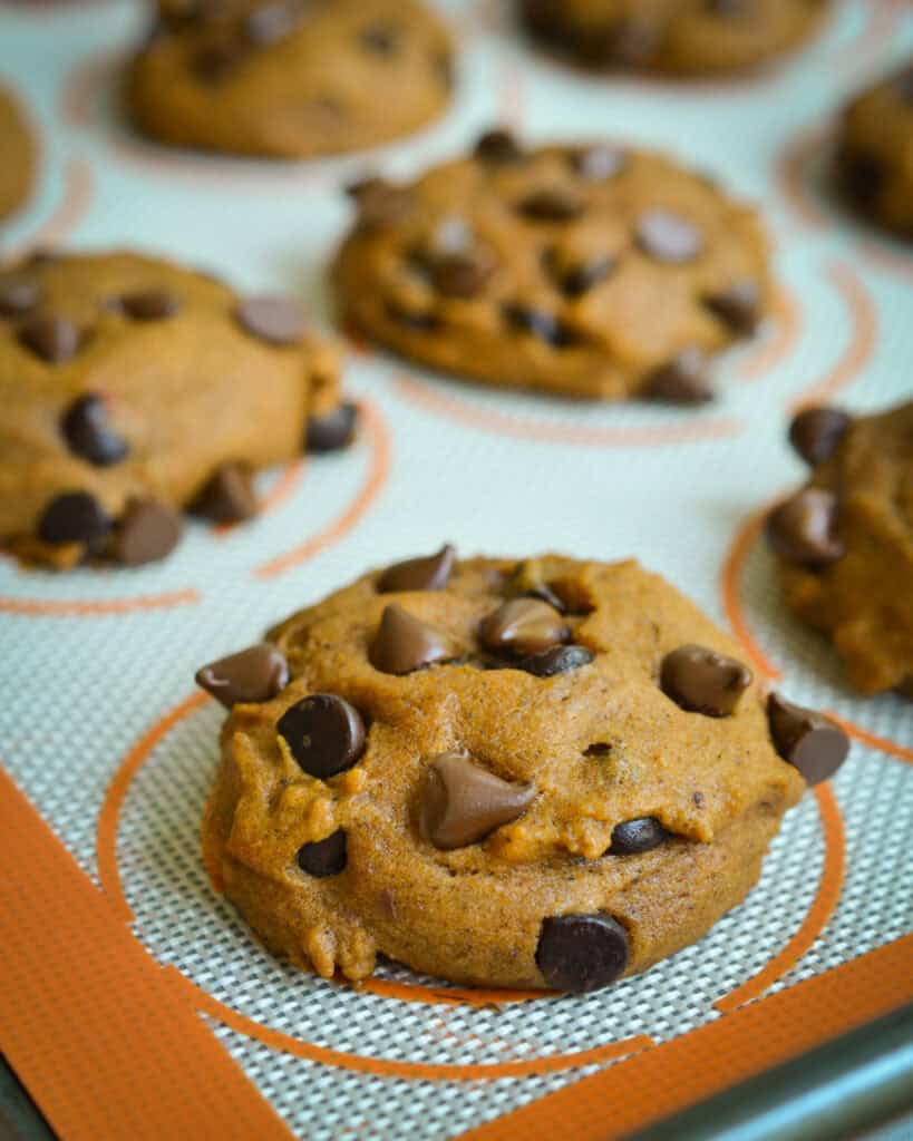 Fresh baked pumpkin chocolate chip cookies on a silicon mat on a baking sheet. 