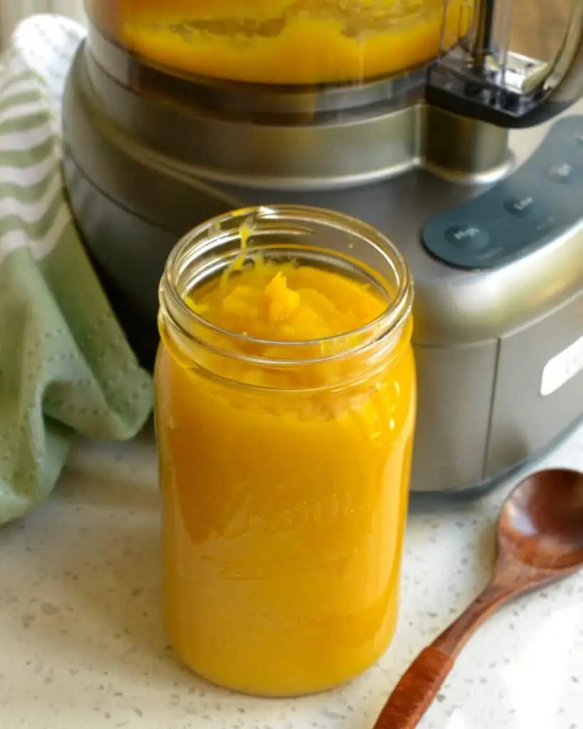 A mason jar full of pumpkin puree in front of a food processor. 