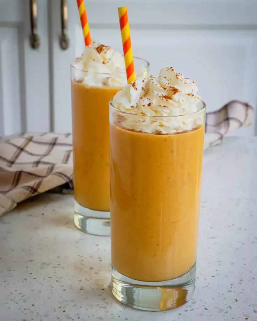 Tall glasses full of pumpkin smoothie topped with whipped cream, cinnamon, and color coordinated straws 