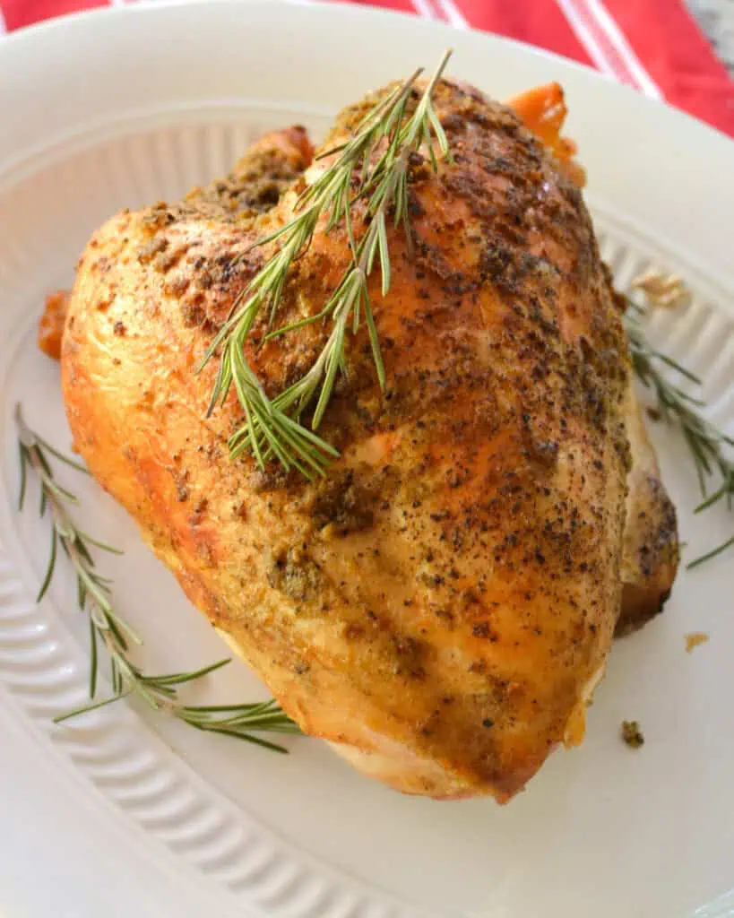 A whole slow cooked turkey breast on a platter with fresh rosemary. 