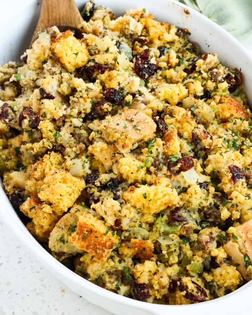 Cornbread stuffing in an oval casserole with a wooden spoon 