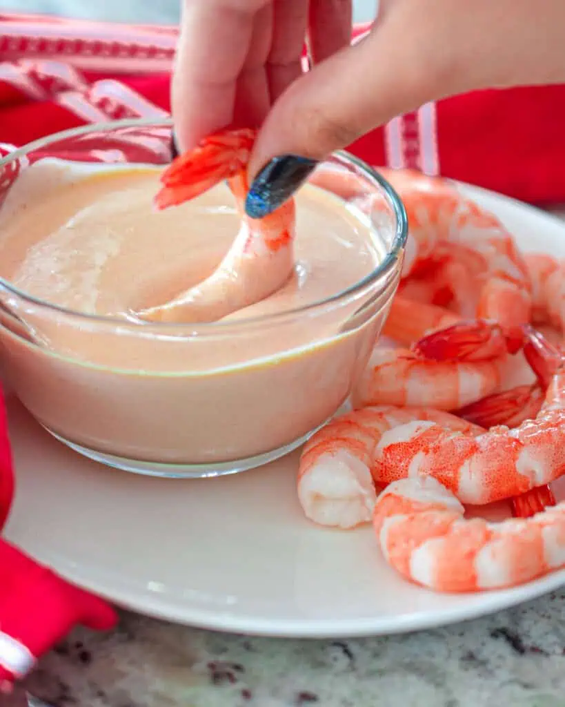 A bowl of yum yum sauce on a plate with steamed shrimp. 