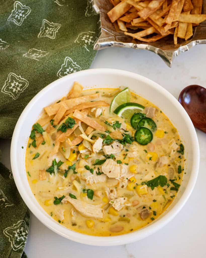 Crockpot white chicken chili in a bowl with chopped cilantro, tortilla strips, jalapeno rings and cheddar cheese. 