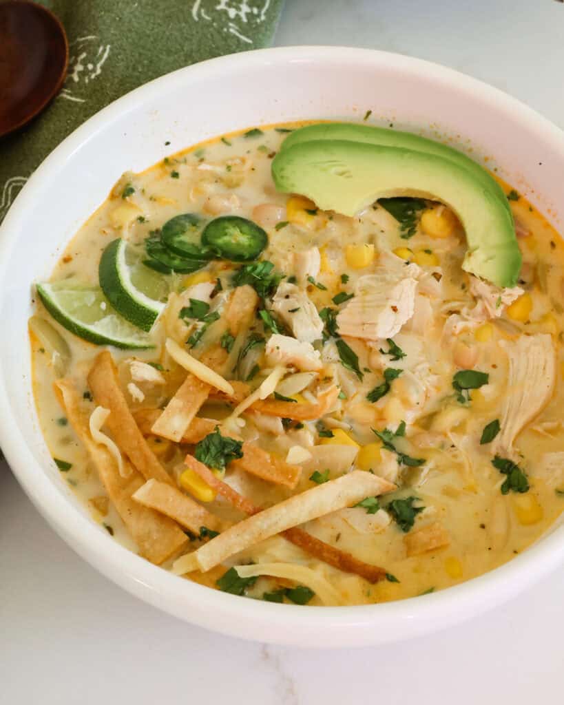 A bowl full of crock pot white chicken chili with tortilla chips, limes slices, jalapeno rings, and avocado. 