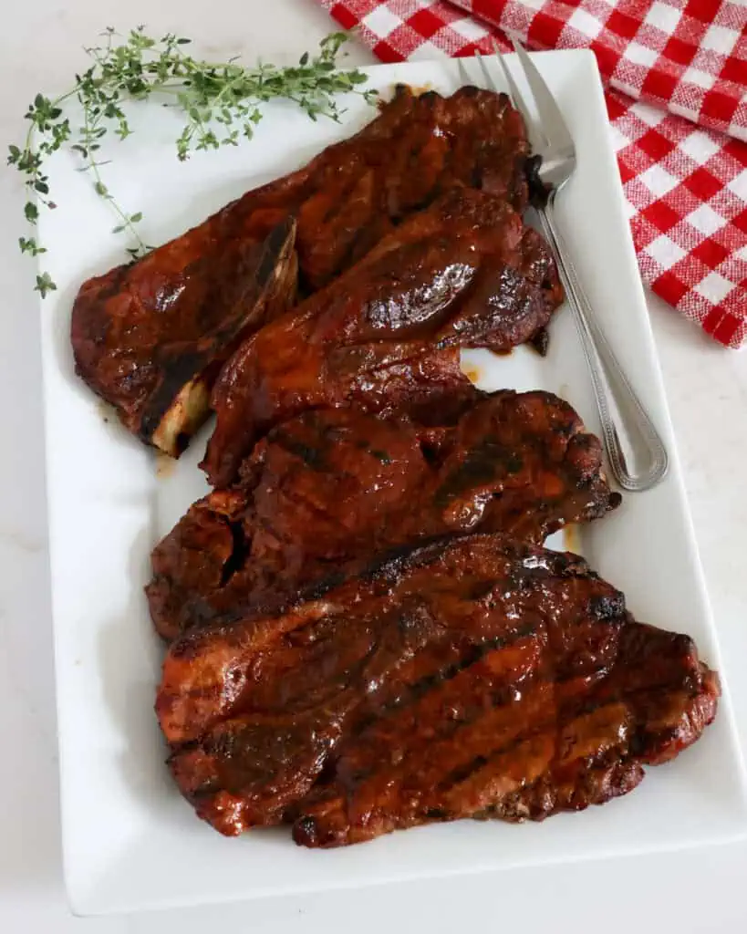 Four pork steaks on a serving platter with a serving fork. 