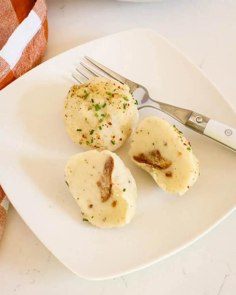 An individual plate with potato dumplings and a fork. One of the potato dumplings is cut in half. 