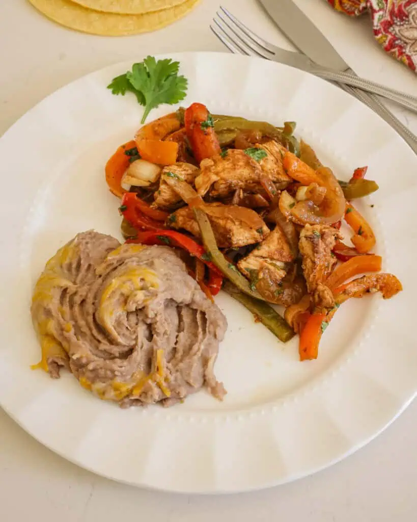 A serving plate with refried beans and chicken fajita mixture. 