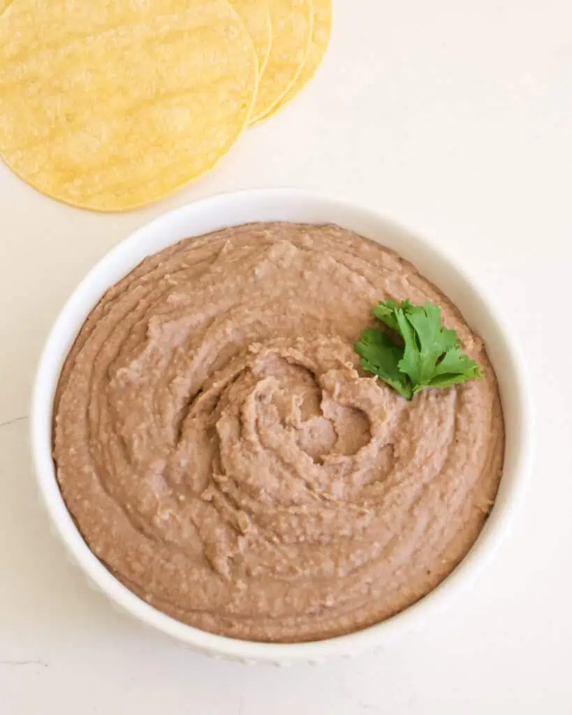 A bowl full of refried beans with corn tortillas in the background. 