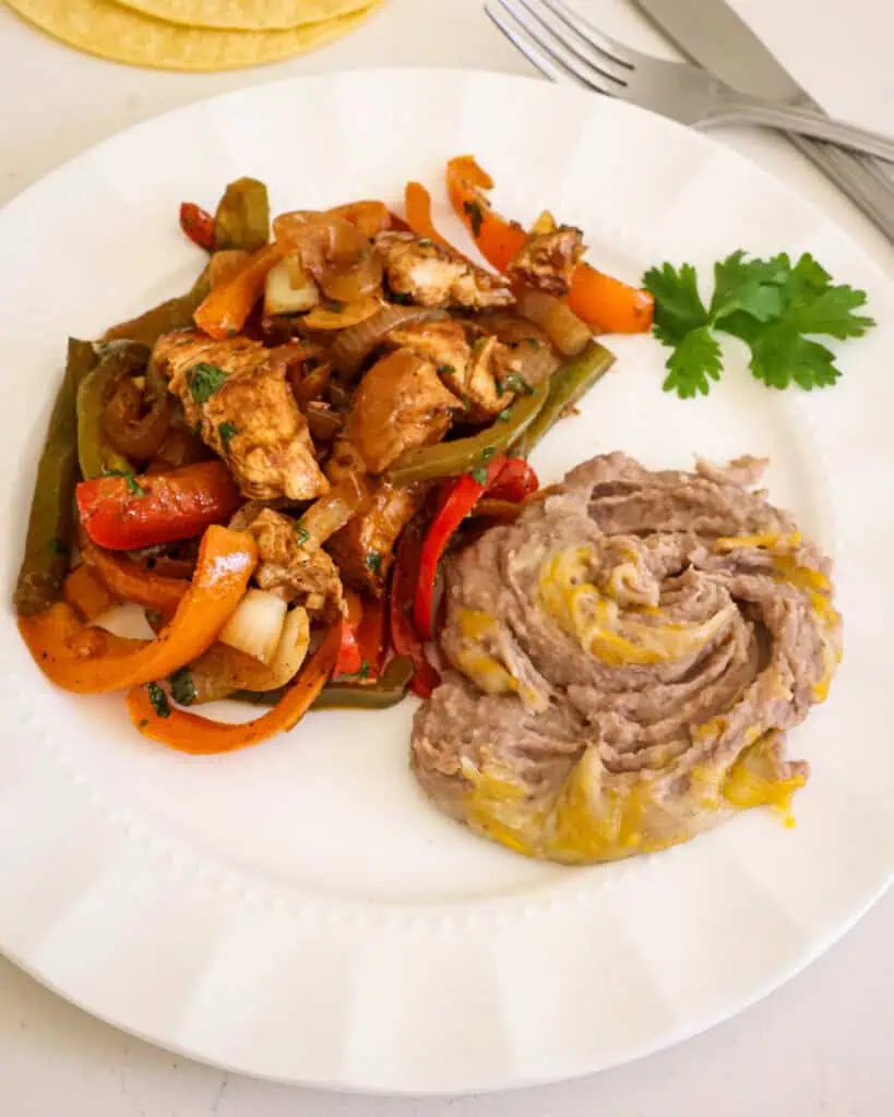 Refried beans and chicken fajita mixture on a serving plate. 