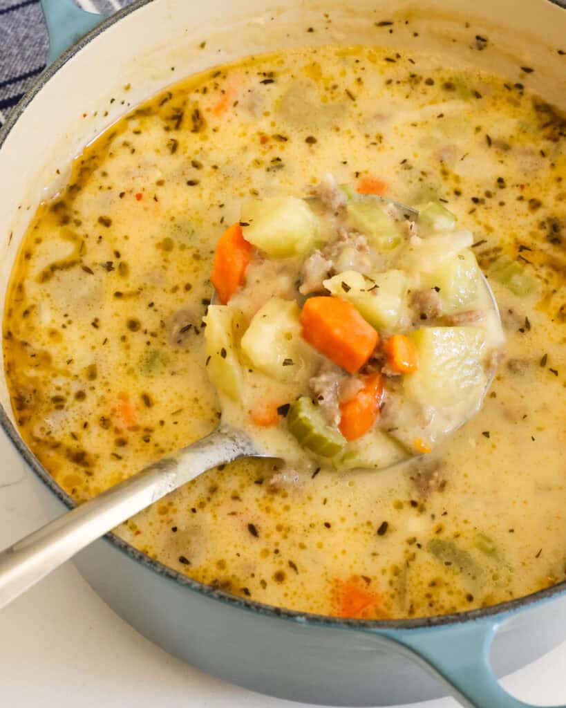 Sausage and potato soup in a Dutch oven with a ladle in it. 