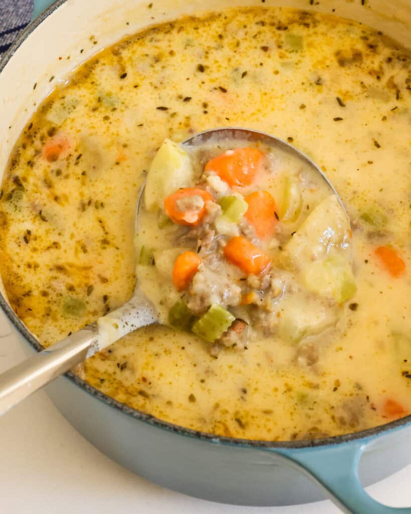 A Dutch oven and ladle full of sausage potato soup. 