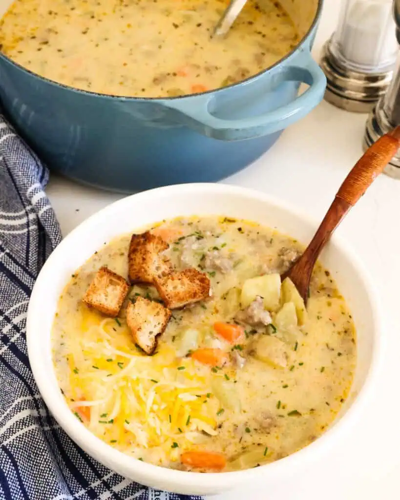 A bowl full of potato and sausage soup with a few croutons and a wooden spoon in the bowl. 