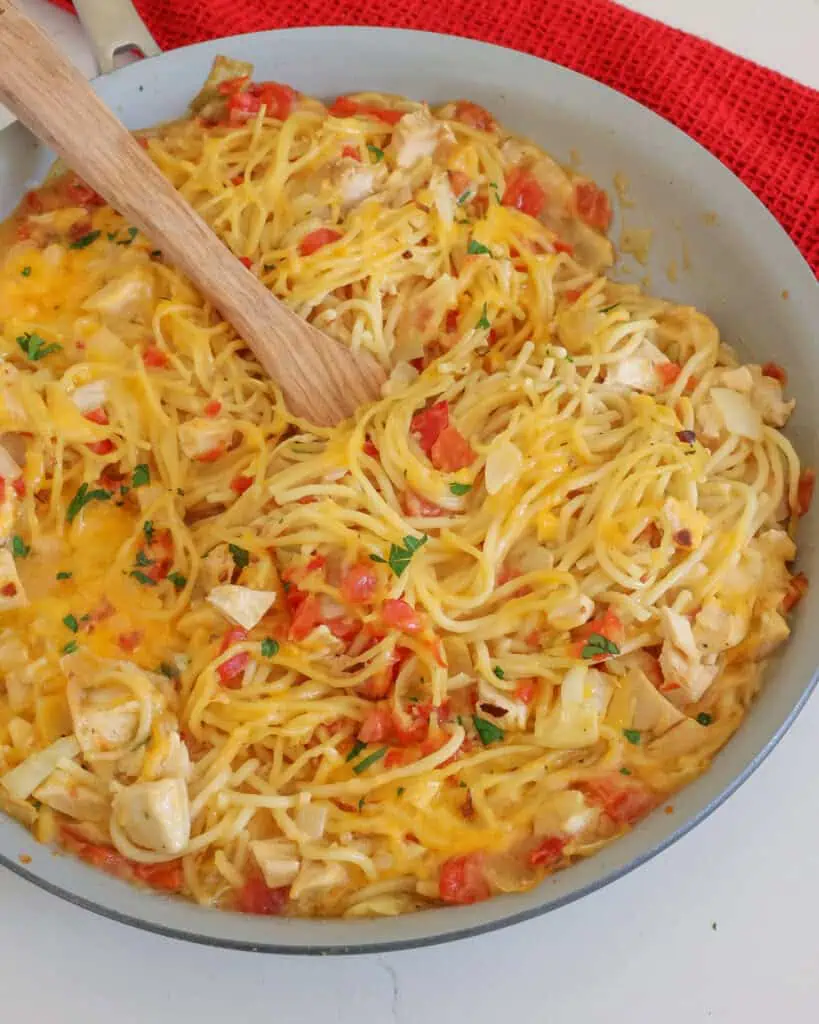 Chicken spaghetti in a large skillet toppeed with shredded cheese and parsley.