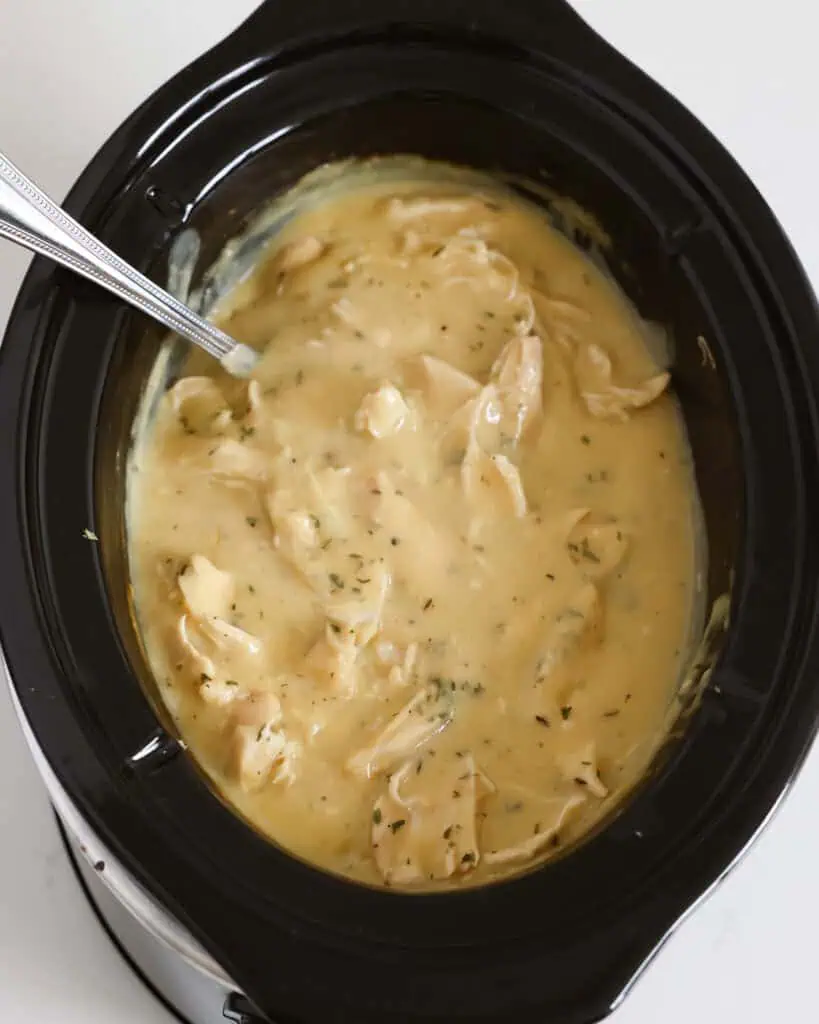 A crockpot full of shrdded chicken and gravy. 