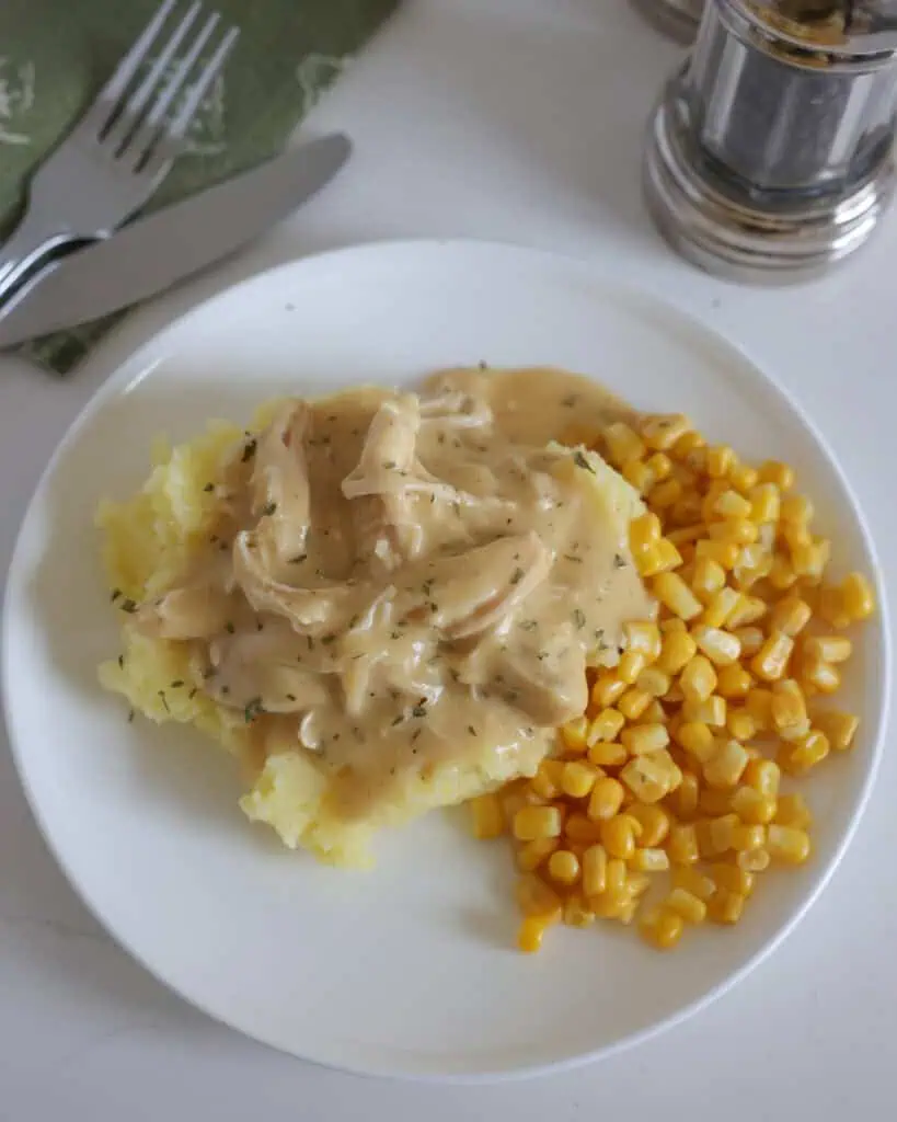 Overhead view of crockpot chicken and gravy with corn on the side on a single serving plate. 