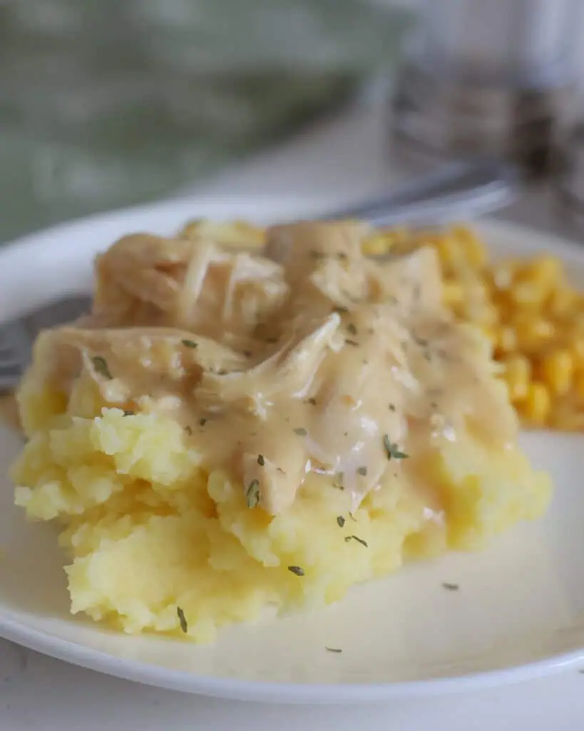 Crockpot chicken and gravy over mashed potatoes with corn on a single serving plate. 