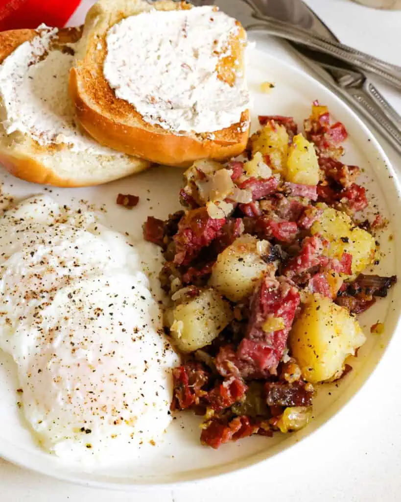 A single serving plate with corned beef hash, poached eggs, and a muffin with butter. 